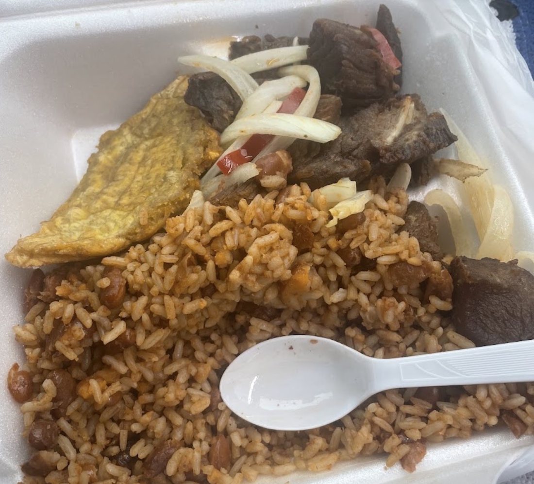 Griot with onions, rice and beans, and fried plantain in a takeout box